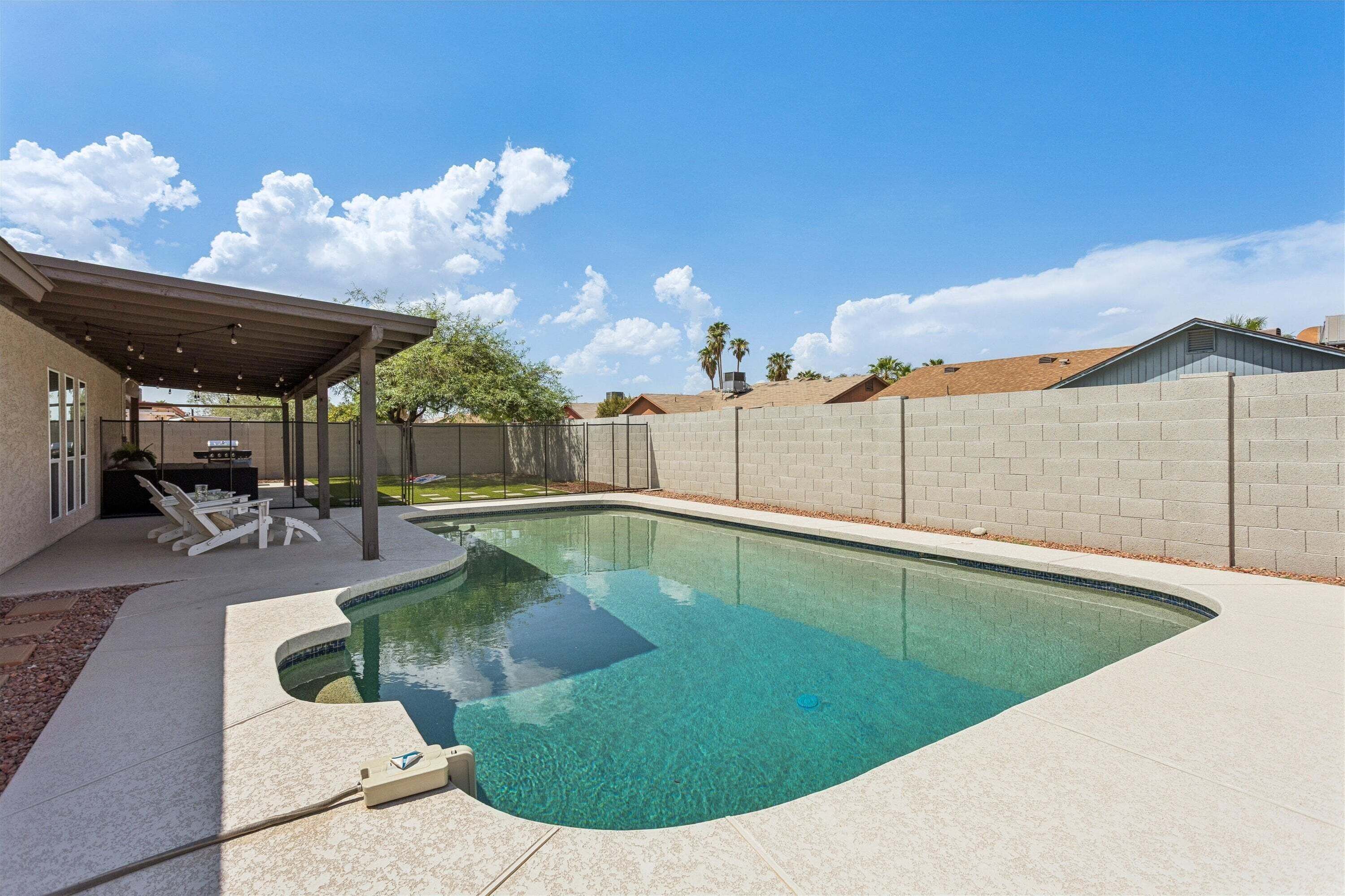 Una piscina con un jacuzzi integrado, un área de patio techada con asientos y un cielo azul despejado.