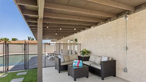 Un patio exterior con piscina, un espacio de estar y una pérgola con luces colgantes.