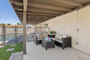 Ein Außenbereich mit einer Poolanlage, einer Sitzgruppe und einem Pergola mit hängenden Lichtern.
