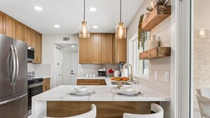 Una cocina moderna con una isla central, electrodomésticos de acero inoxidable, armarios de madera e iluminación colgante.
