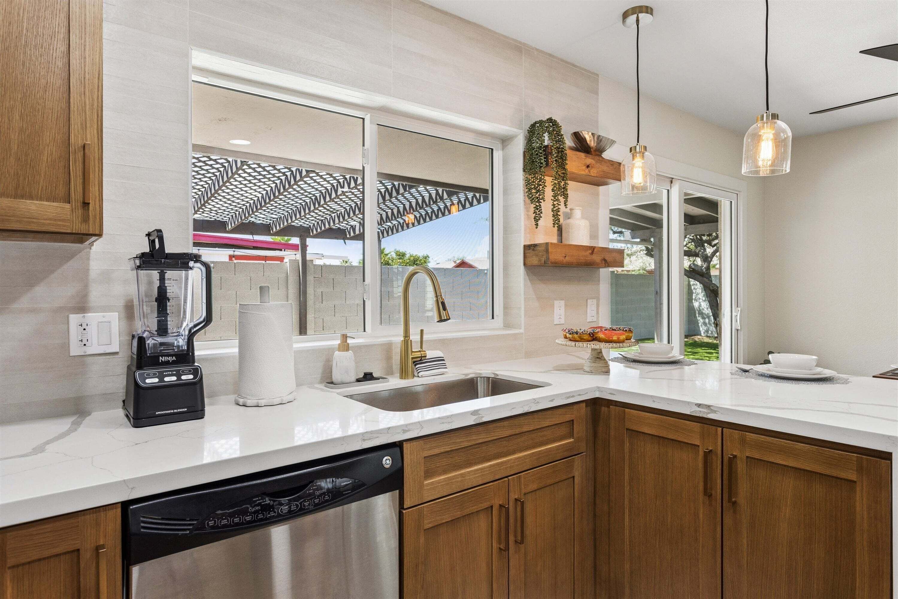 A modern kitchen with a built-in dishwasher, a large window, and a hanging plant.