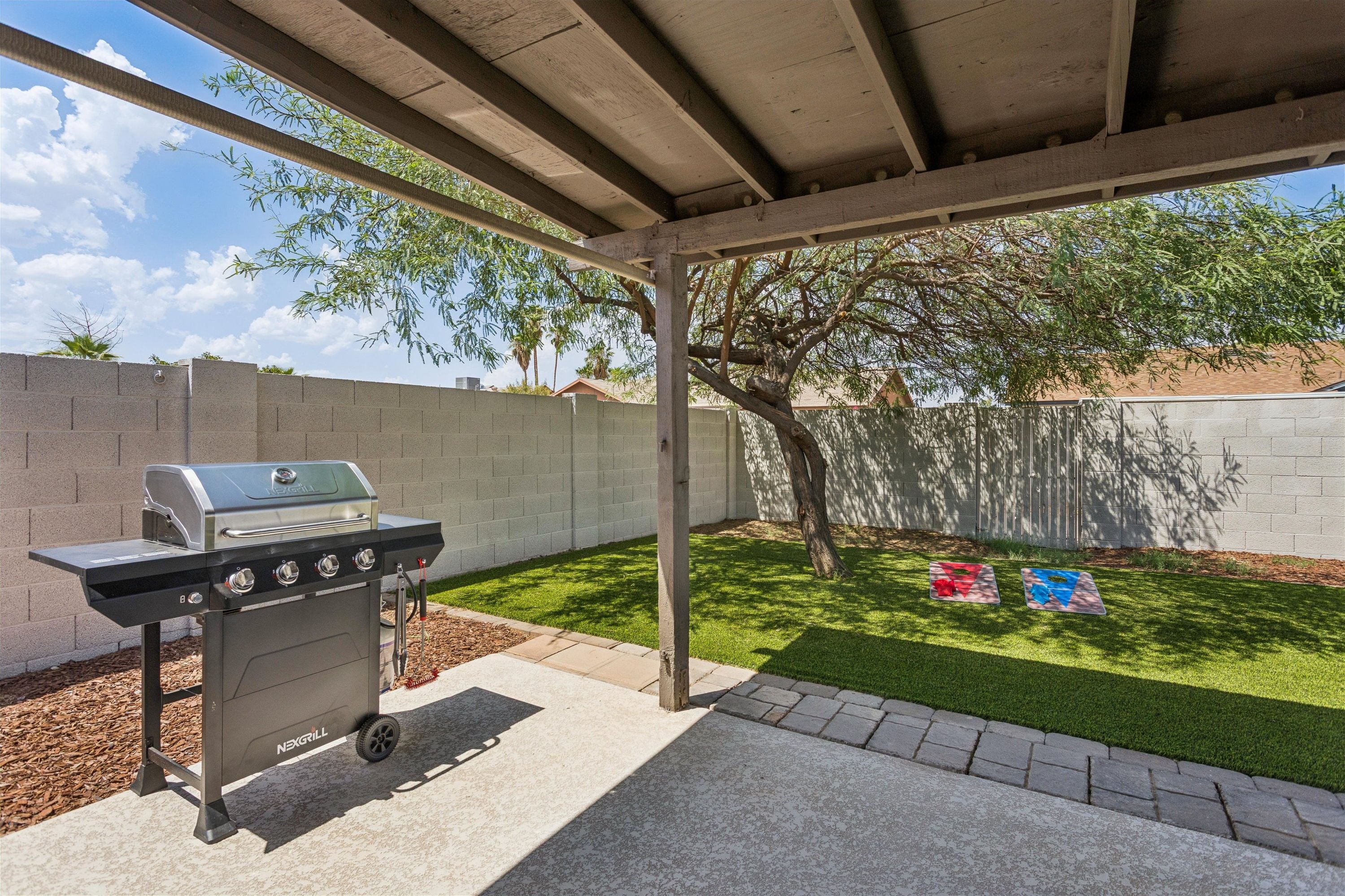 An outdoor barbecue area with a grill, a grassy lawn, and a tree.