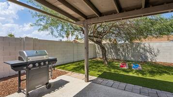 An outdoor barbecue area with a grill, a grassy lawn, and a tree.