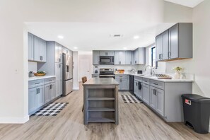 A modern kitchen with grey cabinets, a central island, and a black trash bin. - Sun-Drenched Vegas Retreat w/ Pool & Huge Yard (North Las Vegas)
