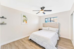 A bedroom with a bed, a ceiling fan, a window, and a wall-mounted shelf with plants. - Sun-Drenched Vegas Retreat w/ Pool & Huge Yard (North Las Vegas)