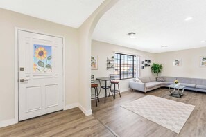 A spacious living area with a large window, a sofa, a dining table, and a kitchen area. - Sun-Drenched Vegas Retreat w/ Pool & Huge Yard (North Las Vegas)