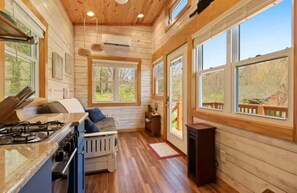 A cabin interior with a kitchen, a dining area, and large windows. - Cozy Teeny Tiny Home with New River view. Pet friendly. (Todd)