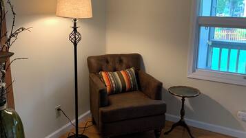 A room with a brown leather armchair, a floor lamp, a small round table, and a window with a view of a fence.