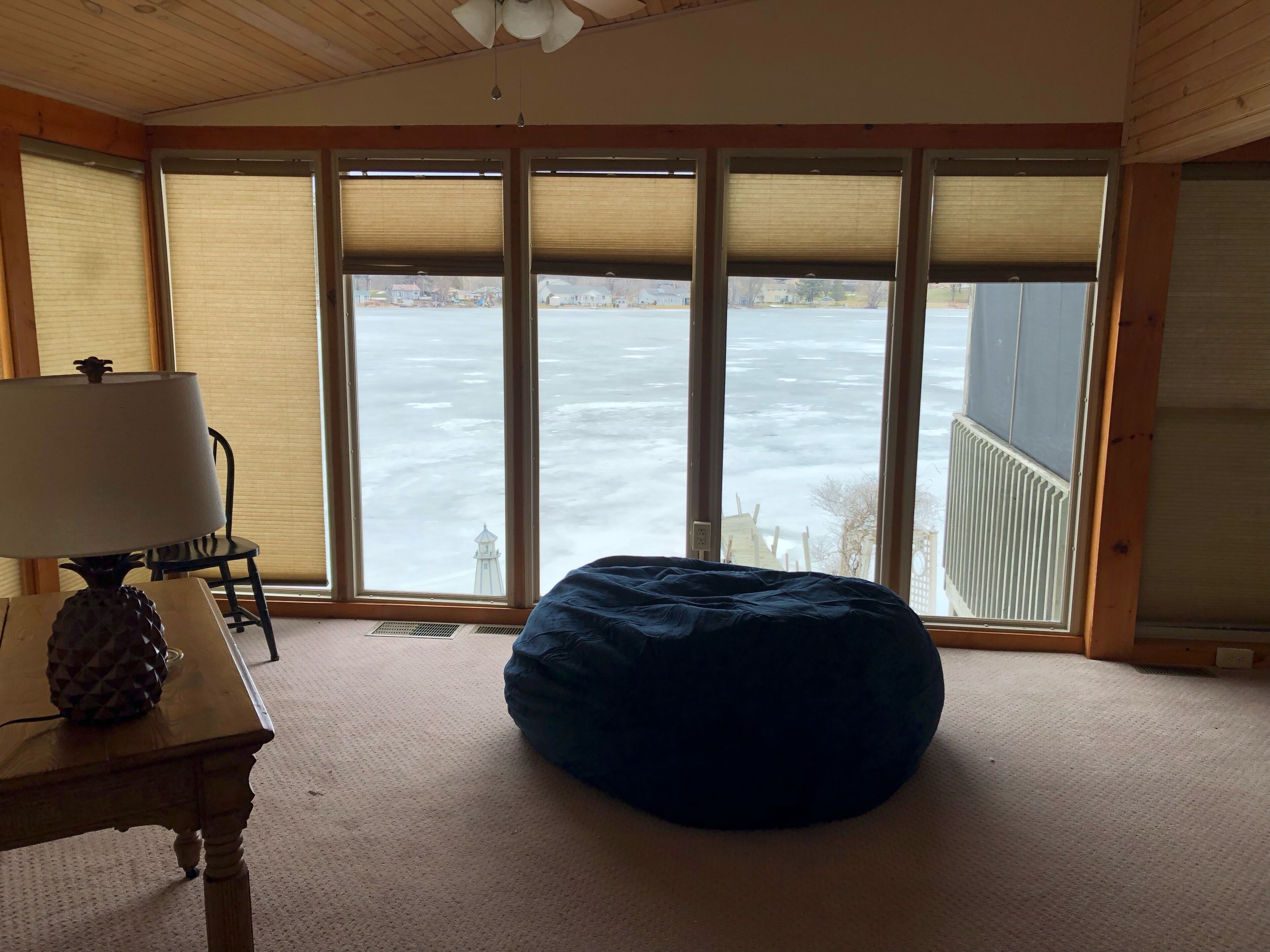 Una habitación con un ventanal grande, una lámpara, una silla y un sillón de plumas.