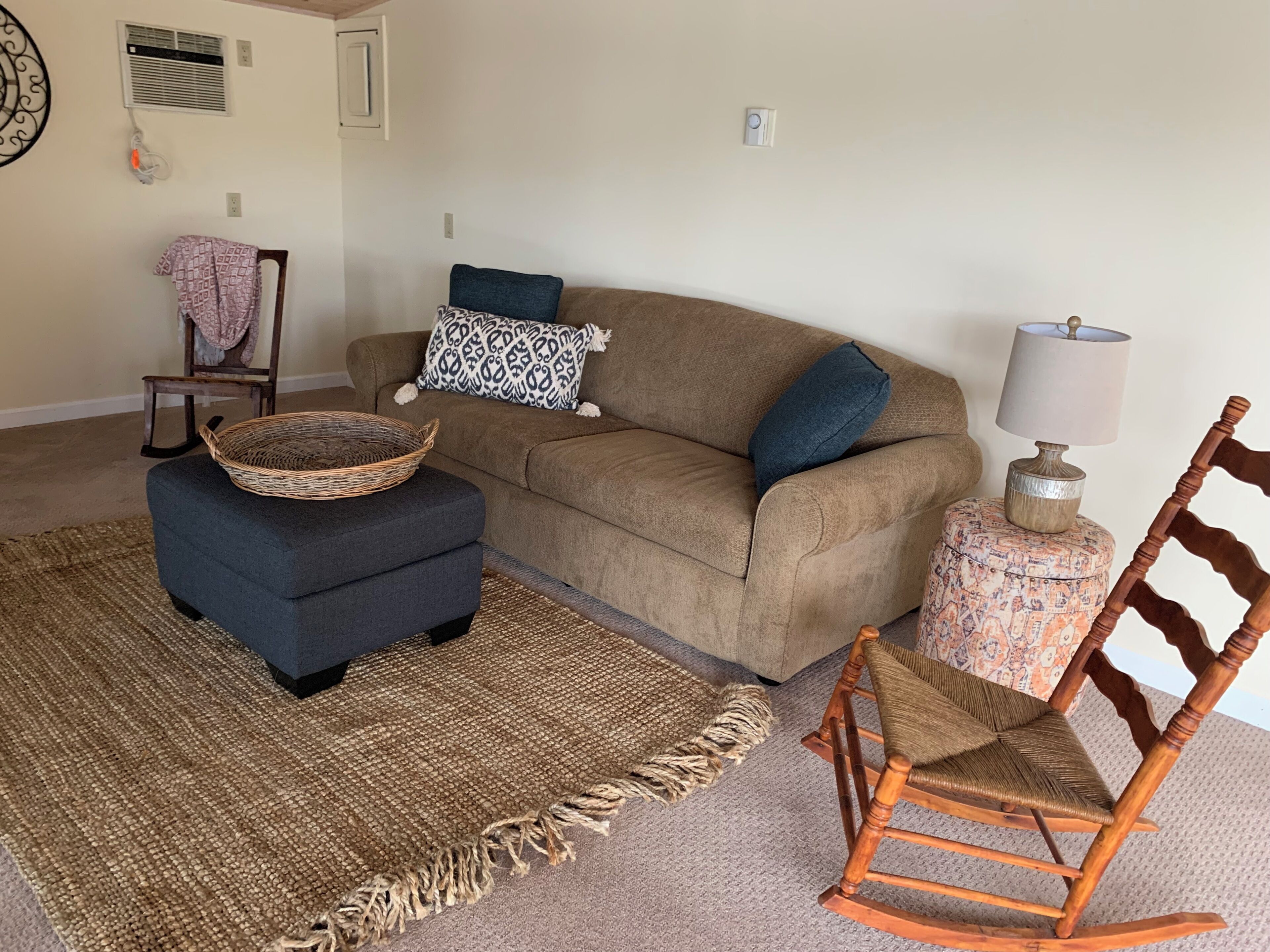 A living room with a sofa, ottoman, rocking chair, and a lamp.