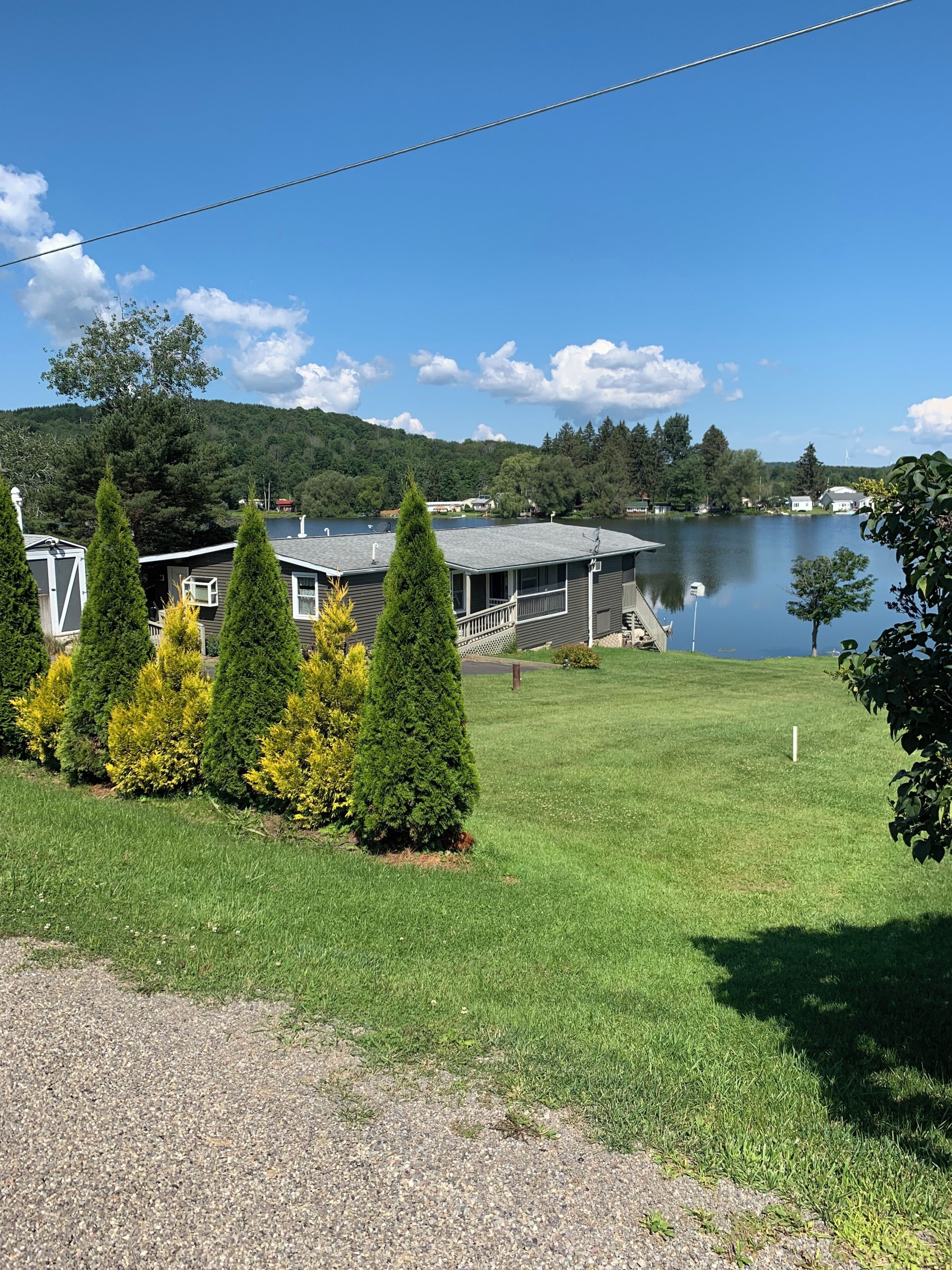 A lakeside property with a grassy lawn, a dock, and a house with a covered porch.