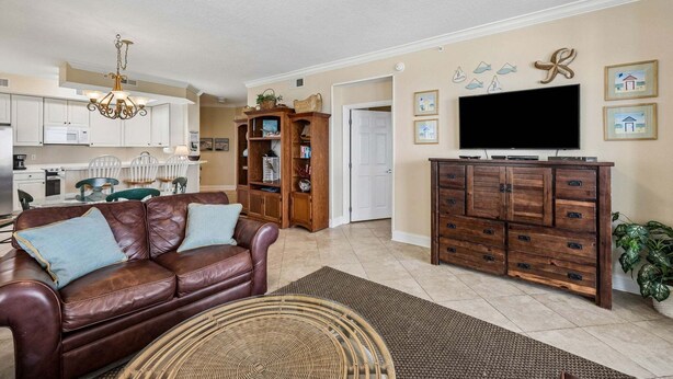 A living room with a leather sofa, a wooden entertainment center, and a dining area with white chairs. - Oceanfront, Bottom Floor condo with pool, balcony, washer/dryer (Fernandina Beach)