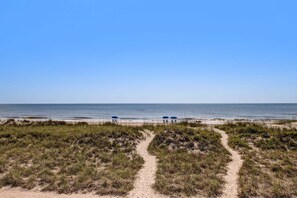 Ein Strandweg führt zum Meer, vorbei an Dünen und Strandstühlen.