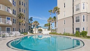 A swimming pool with lounge chairs, surrounded by palm trees and a building with balconies. - Oceanfront, Bottom Floor condo with pool, balcony, washer/dryer (Fernandina Beach)