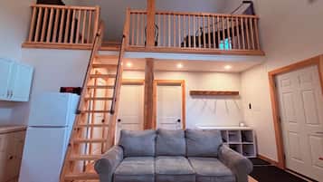 A loft-style living space with a wooden staircase, a sofa, a kitchenette, and a small dining area.