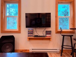 A room with a mounted television, wooden shelves with DVDs, a speaker, and a table.