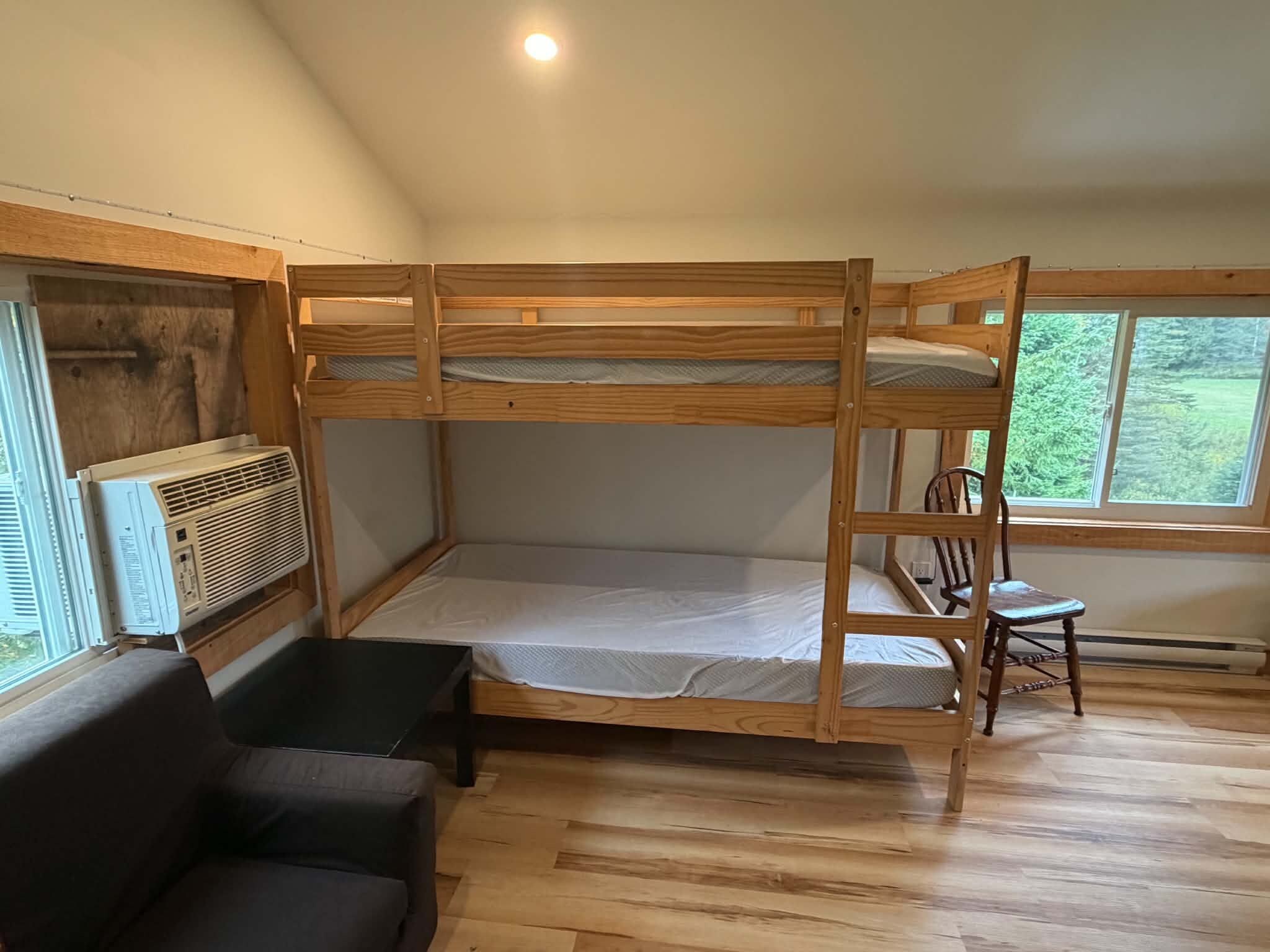 A bunk bed room with a wooden floor, a window, and a chair.