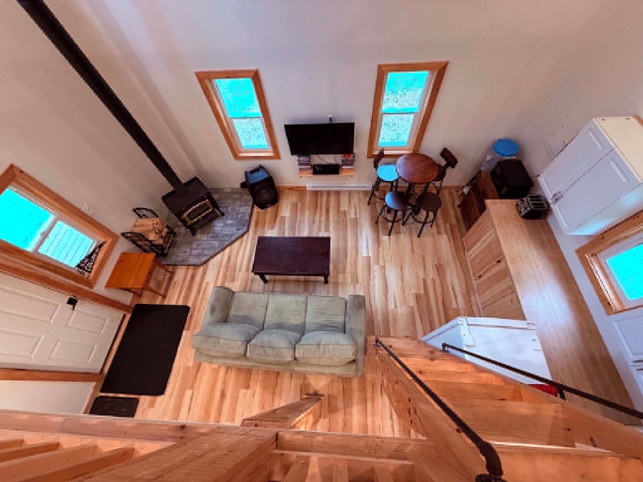 A spacious living area with a wooden floor, a sofa, a TV, and a dining table with chairs.