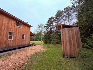 A wooden house with a shed, surrounded by trees and a gravel path.
