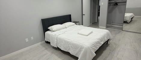 A modern bedroom with a large bed, a walk-in closet, and a full-length mirror.