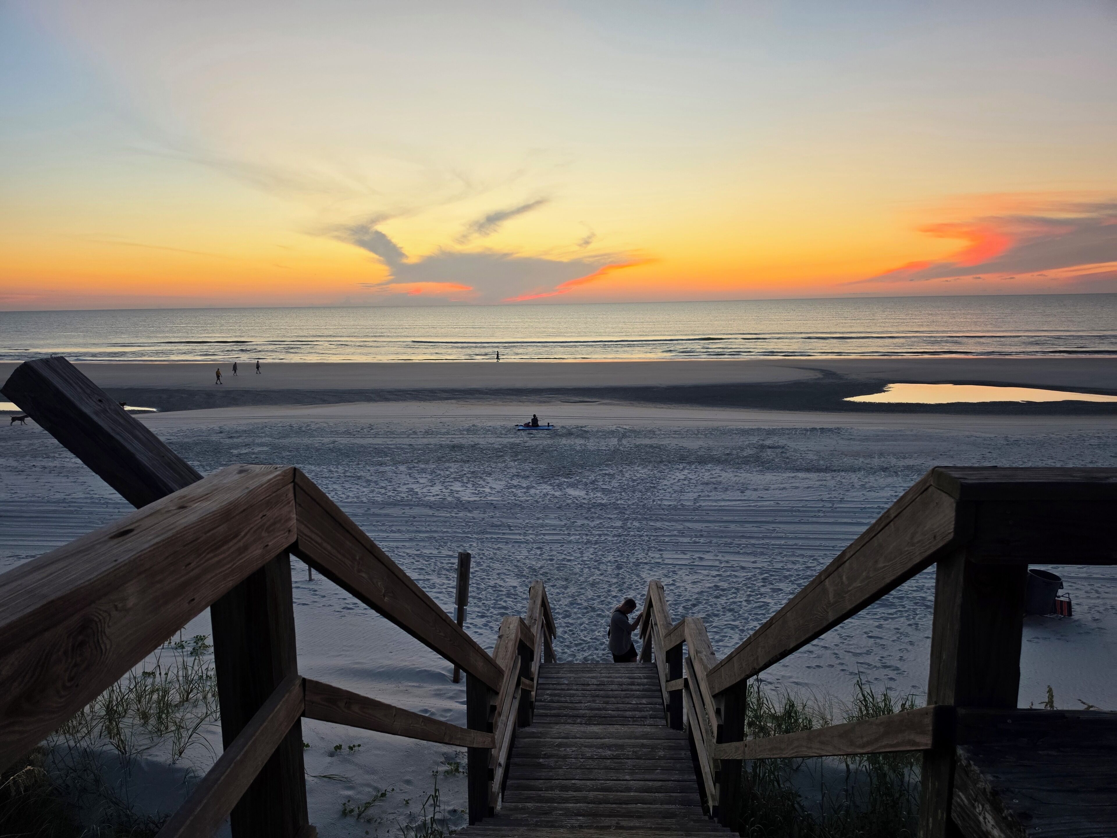 A wooden staircase leading to a beach with a sunset in the background.