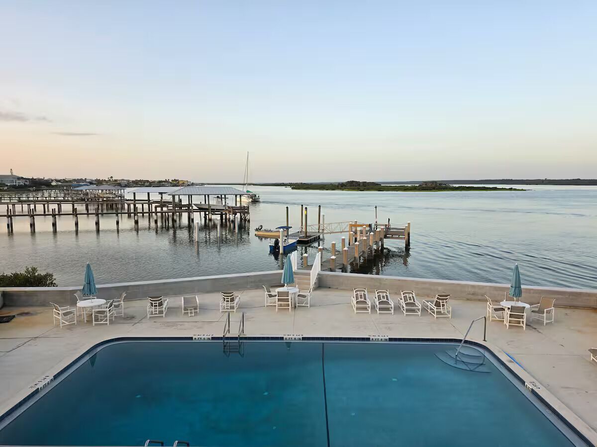 A pool area with lounge chairs and a view of a pier extending into the water.