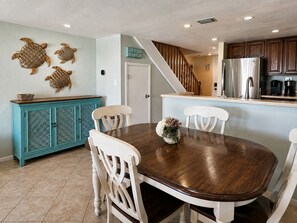 A dining area with a wooden table and white chairs, a turquoise cabinet with decorative patterns, and a kitchen with wooden cabinets and a stainless steel refrigerator. - Waterfront views • Walk to Beach • Riverfront pool • Dog-friendly (St. Augustine)