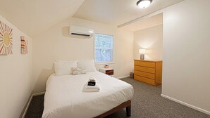A bedroom with a bed, an air conditioning unit, a nightstand, a dresser, and a lamp. - Spacious 4 Bedroom Extended Stay Home | Pet Friendly (Newberg)
