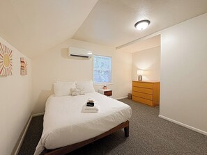 Ein Schlafzimmer mit einem Bett, einer Klimaanlage, einem Nachttisch, einer Kommode und einer Lampe.