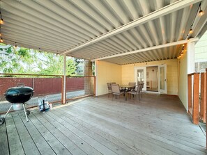 Ein überdachter Patio-Bereich mit Grill, Esstisch und Stühlen.