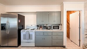 A compact kitchen with a refrigerator, stove, microwave, and grey cabinets. - Spacious 4 Bedroom Extended Stay Home | Pet Friendly (Newberg)