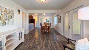 A hallway with a dining area, a TV in the background, and a door leading to another room. - Spacious 4 Bedroom Extended Stay Home | Pet Friendly (Newberg)