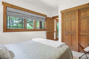 A bedroom with a bed, a window with a view of greenery, and a wooden door. - Brand-New Feel 3BR + Loft | Private Hot Tub, Ski Views & Garage | Steps to Free Bus (Steamboat Springs)