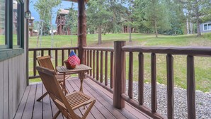 En träaltan med ett bord och stolar, med utsikt över en gräsyta med träd och en byggnad i bakgrunden.
