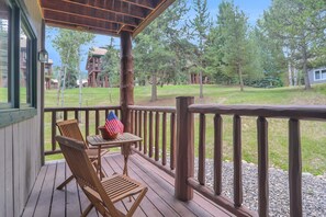 Eine Holzterrasse mit Tisch und Stühlen, mit Blick auf eine Rasenfläche mit Bäumen und einem Gebäude im Hintergrund.