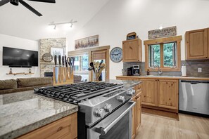 Eine moderne Küche mit Gasherd, Edelstahlgeräten, Holzschränken und einer Küchenrückwand aus Stein.