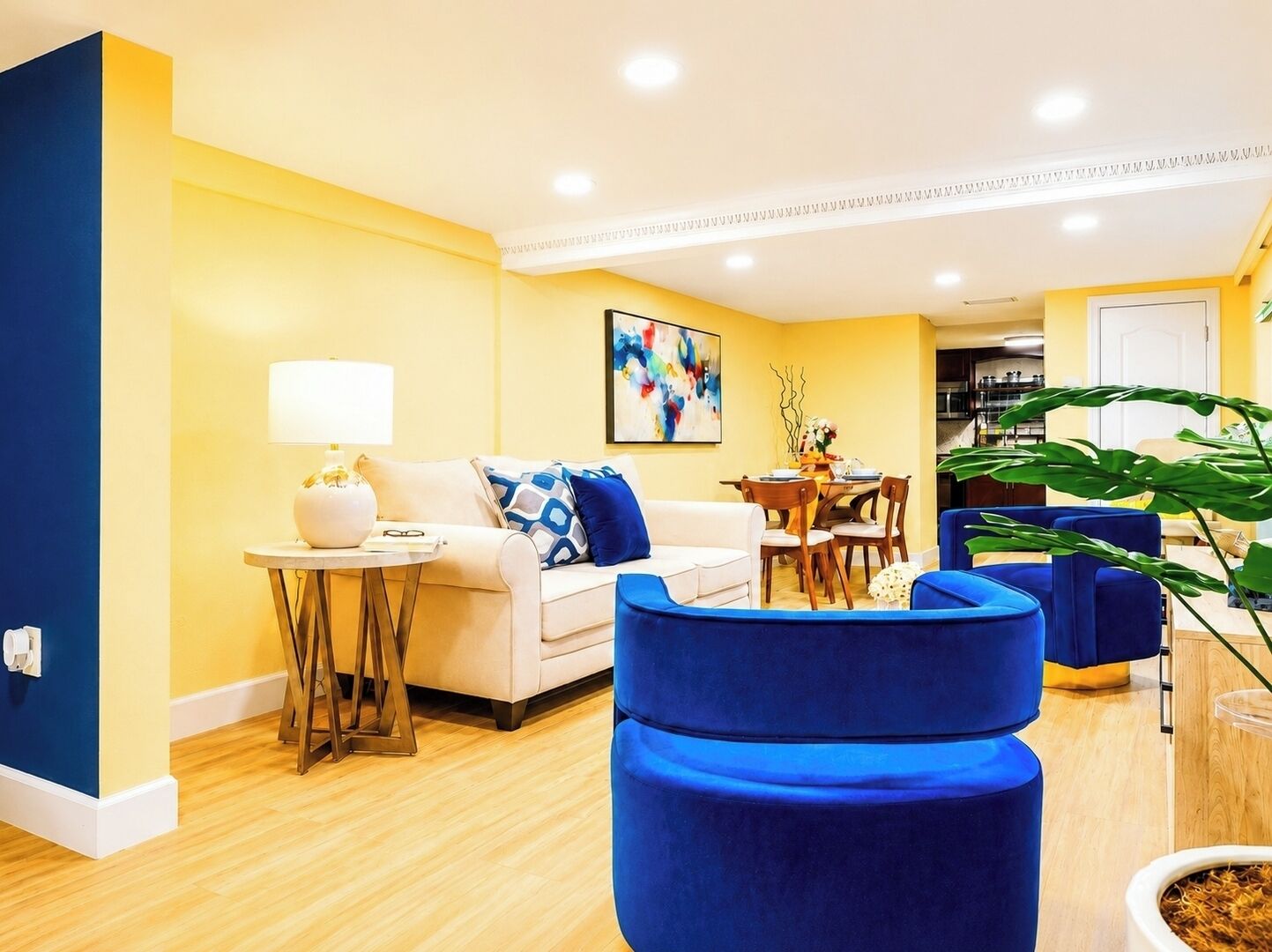 A modern living room with a sofa, a table with a lamp, and a dining area with chairs.
