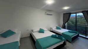 Habitación de hotel con dos camas, una ventana con cortinas, un equipo de aire acondicionado y vistas al exterior.