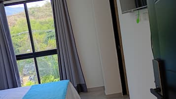 Una habitación de hotel con cama, ventana con cortinas, puerta y televisor montado en la pared.