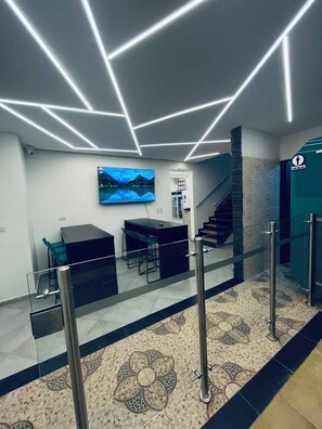 Un lobby moderno con una mesa de recepción, zona de estar y una escalera.