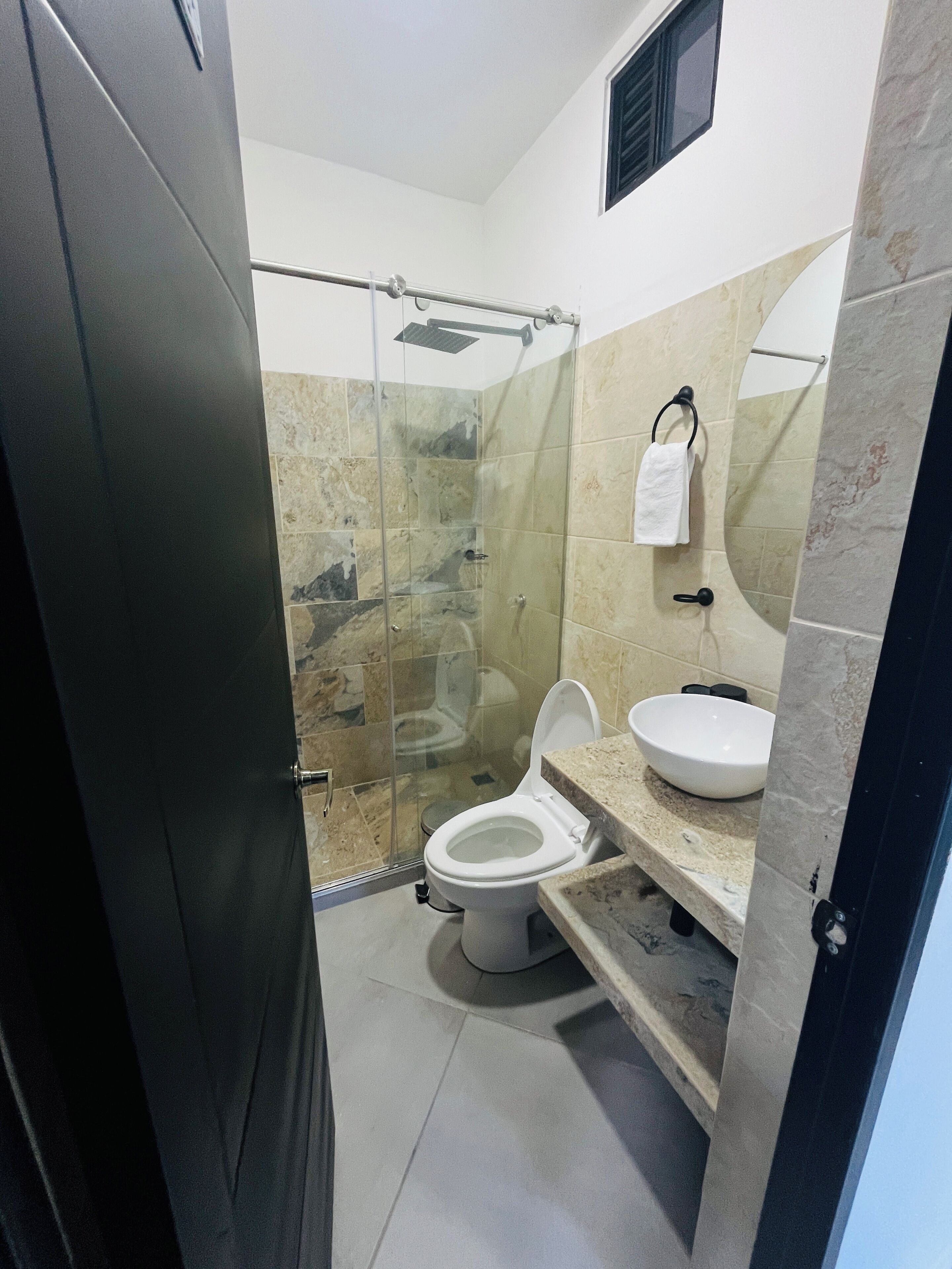 A bathroom with a glass-enclosed shower, a toilet, and a sink with a marble countertop.