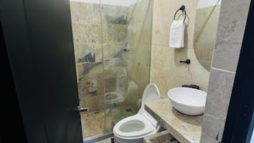 A bathroom with a glass-enclosed shower, a toilet, and a sink with a marble countertop.