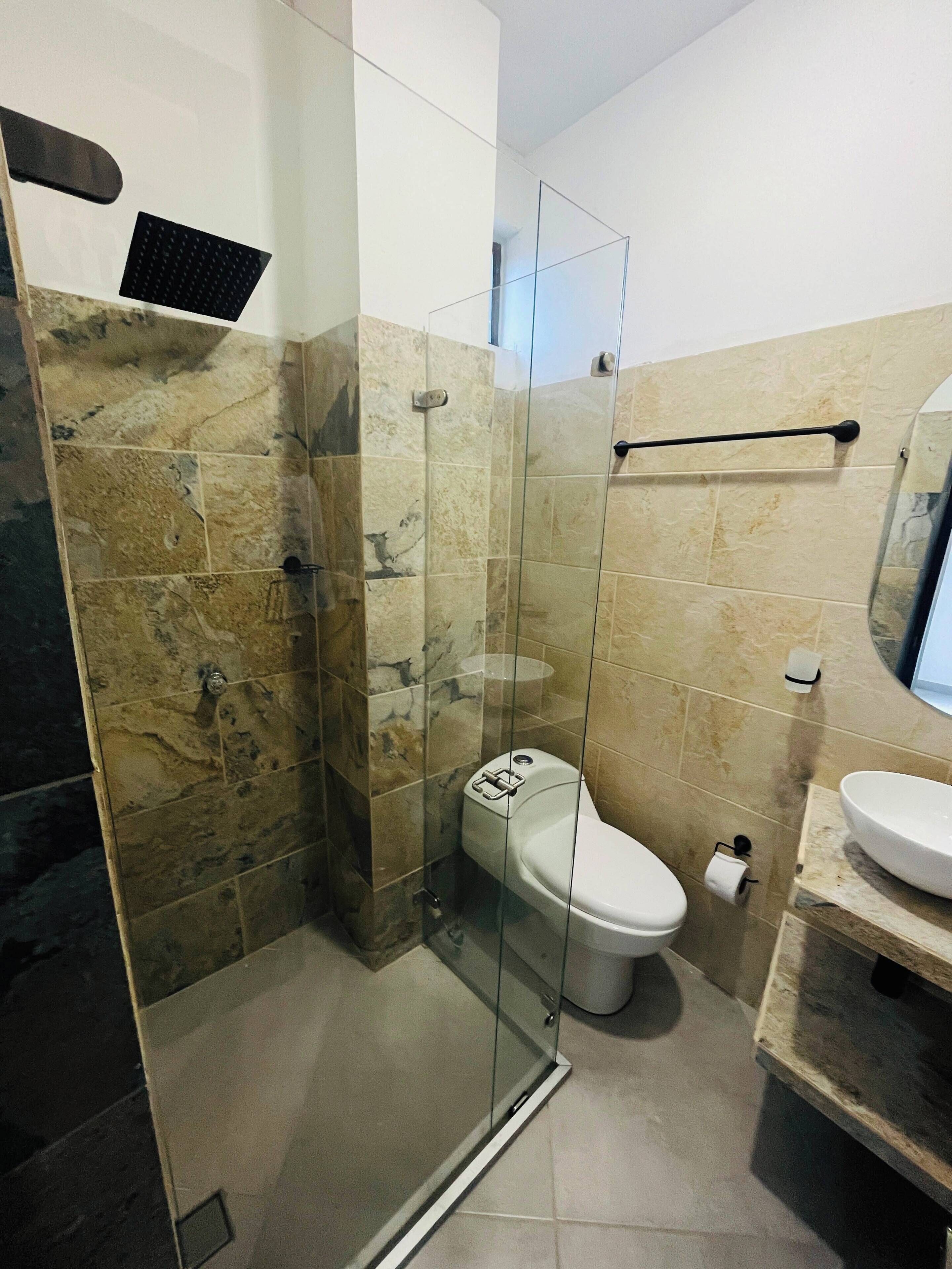 A bathroom with a glass-enclosed shower, a toilet, and a sink.