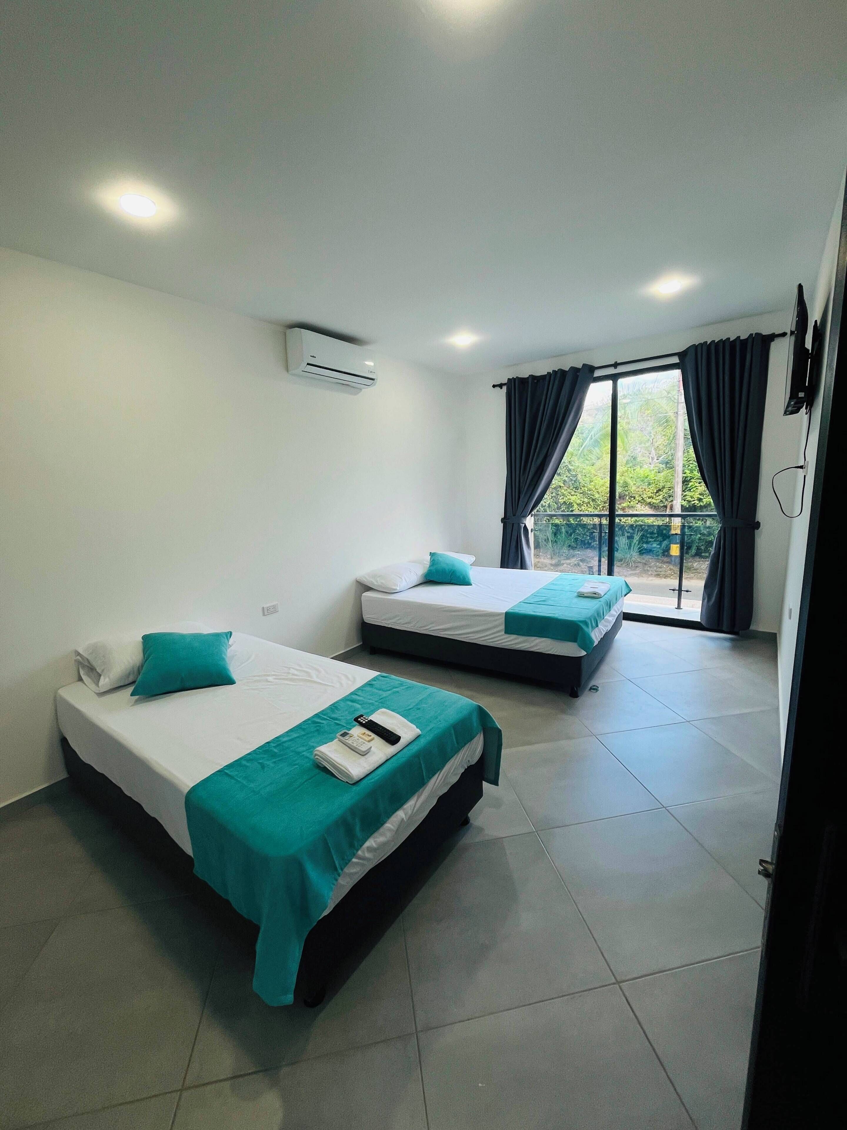 A hotel room with two beds, a TV, and a sliding glass door to the outside.