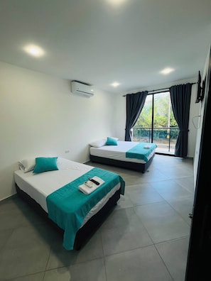 Habitación de hotel con dos camas, televisión y puerta corrediza al exterior.