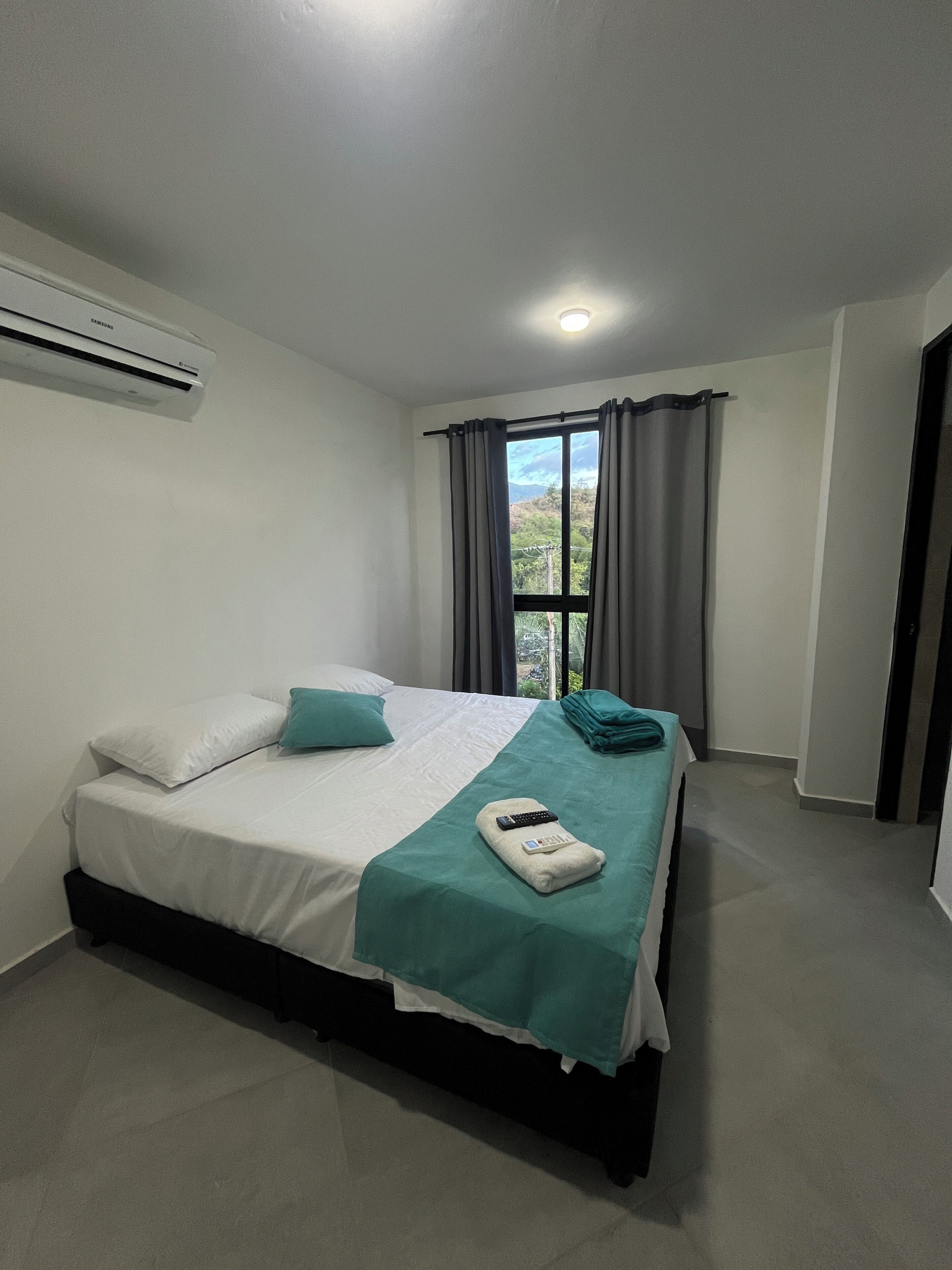 Habitación de hotel con una cama, un control remoto y una ventana con cortinas.
