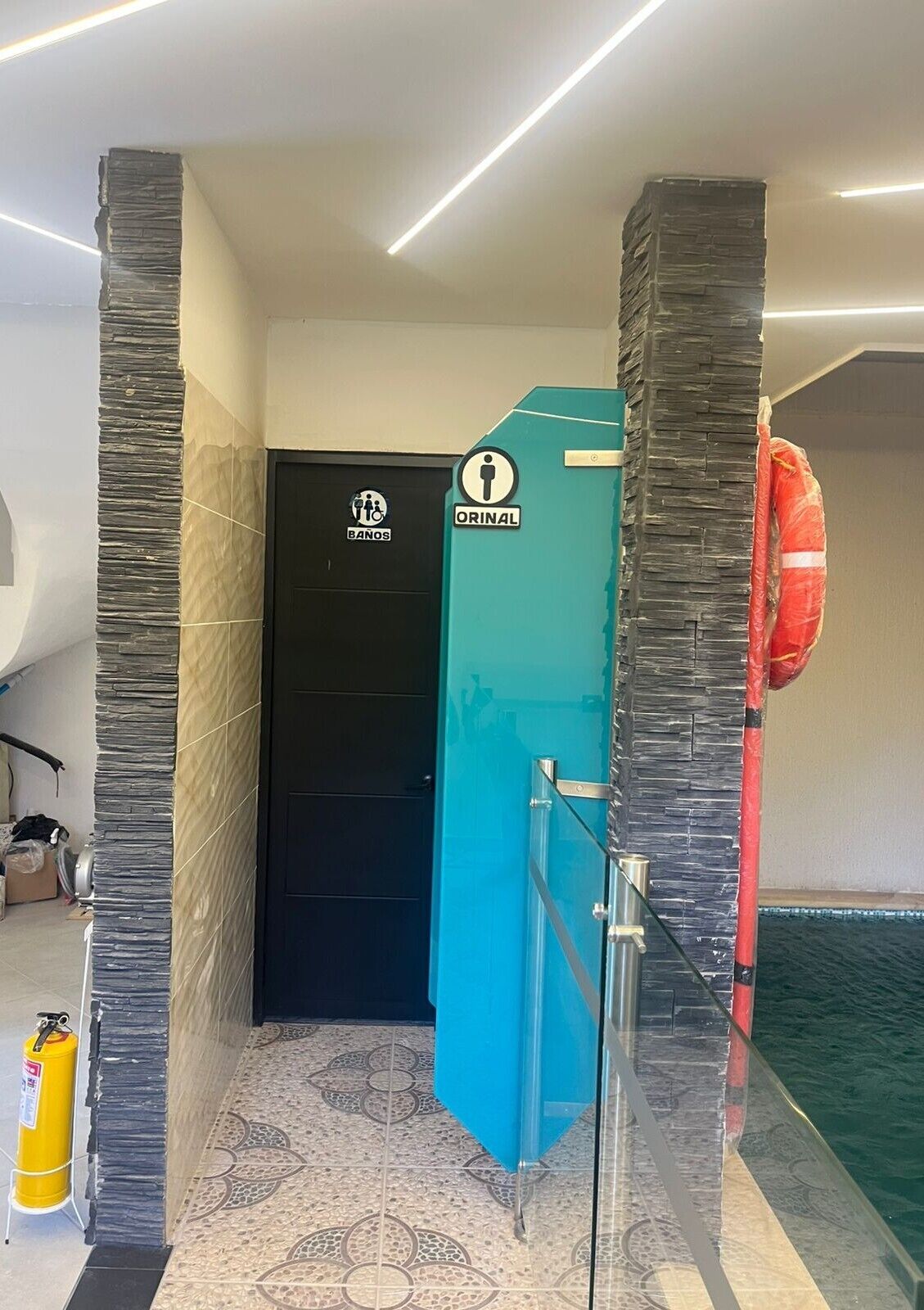 Une salle de bain avec une porte noire, un box bleu et une bouée rouge.