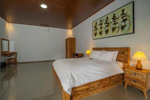 A bedroom with a wooden bed, bedside lamps, a wooden wardrobe, a desk with a chair, and a painting on the wall.
