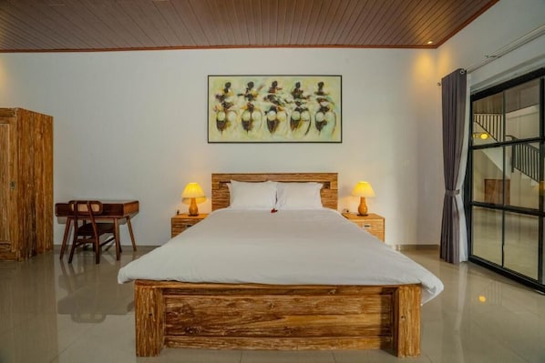 A bedroom with a wooden bed, bedside lamps, a desk, and a large window.