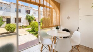 Un balcón con una mesa y sillas blancas, una planta en maceta y vistas a un patio con edificios.
